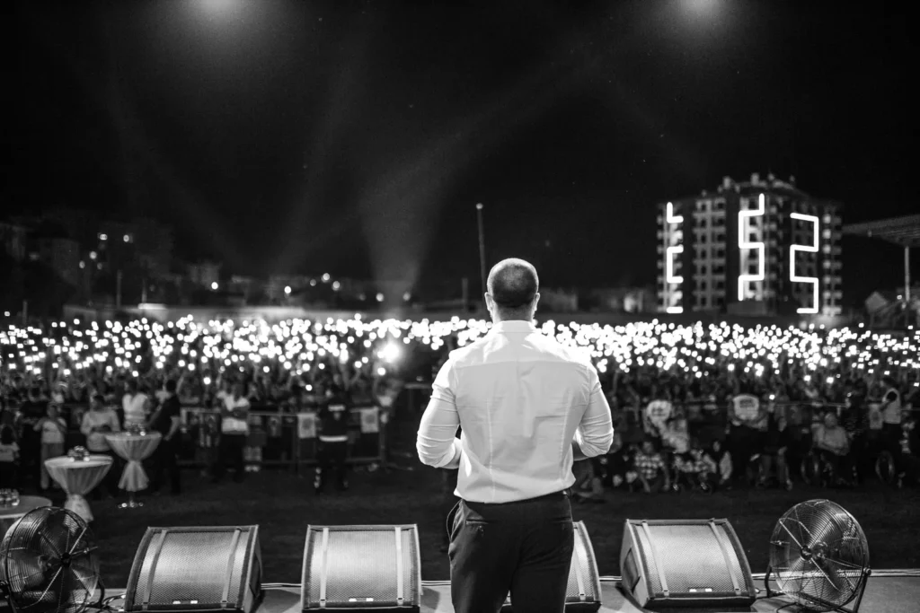 Palestrante no palco diante de multidão em evento noturno